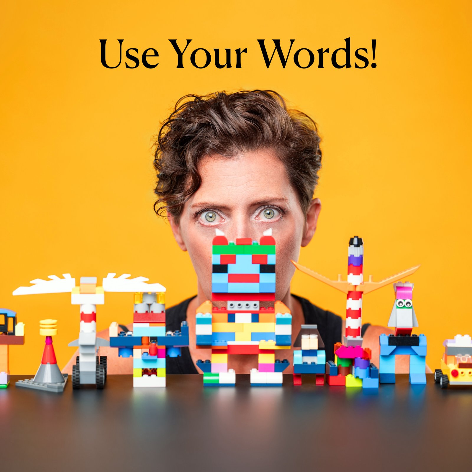 woman in front of yellow background and behind a table of legos